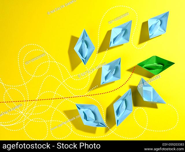 a group of blue paper boats and one green with paths on a yellow background. The concept of a strong leader with extraordinary thinking, quick decision-making