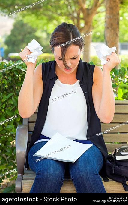 Frustrated and Upset Young Woman with Pencil and Crumpled Paper in Her Hands Sitting on Bench Outside