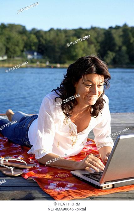 A woman with a laptop on a jetty by a lake, Sweden