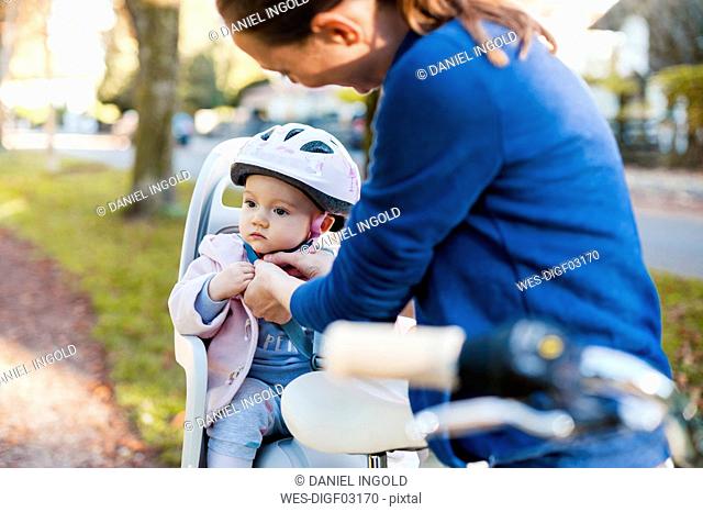 Mother and daughter riding bicycle, baby wearing helmet sitting in children's seat