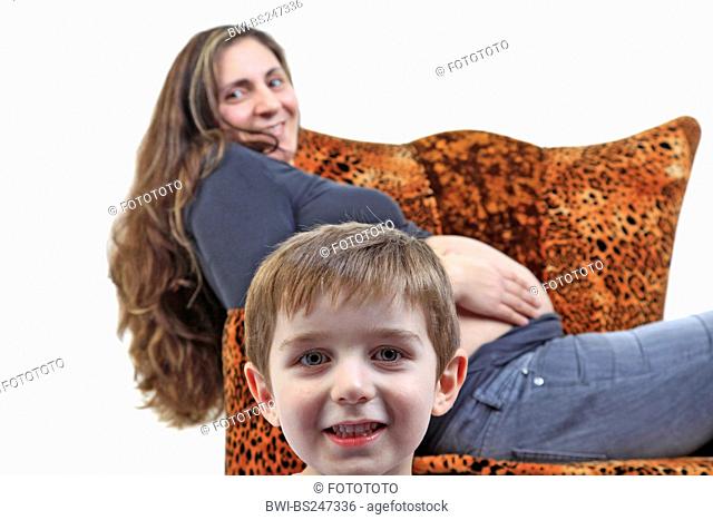 pregnant mother sitting in a leopard armchair holding her bare belly, the head of her son in the foreground