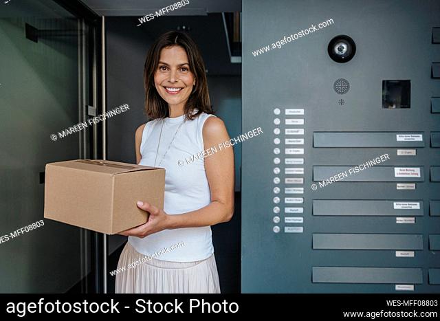 Smiling woman holding package standing at door
