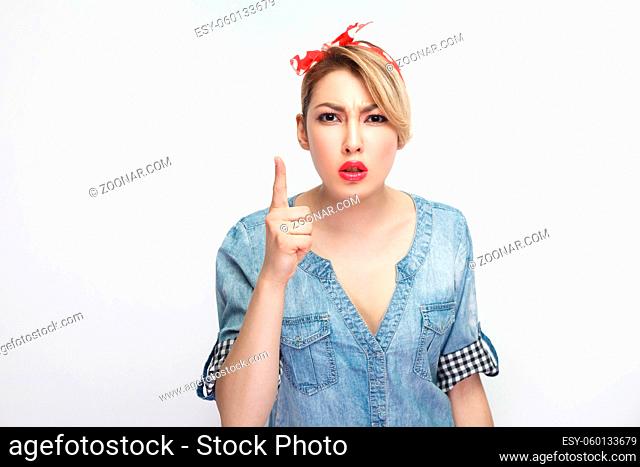 Portrait of attention serious beautiful young woman in casual blue denim shirt with makeup and red headband standing warning and looking at camera