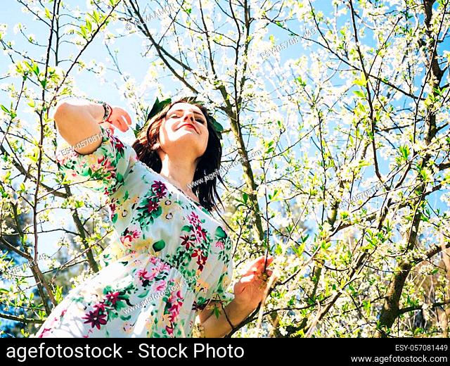 Young beautiful woman in bay leaf wreath dreaming with closed eyes in spring blossom cherry garden