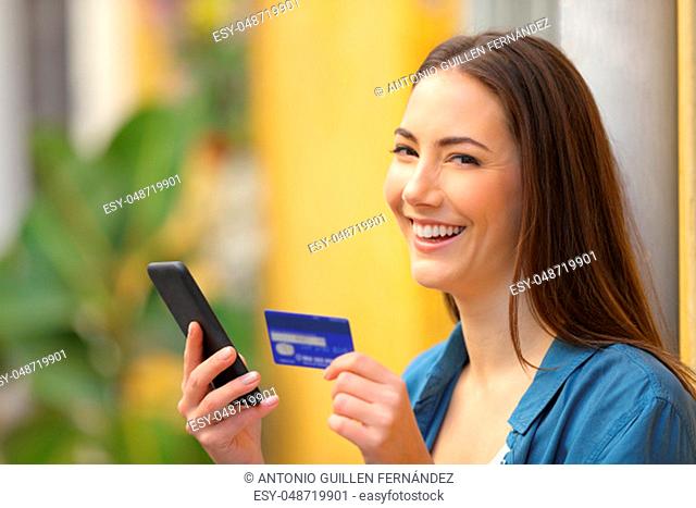 Happy buyer buys on line with credit card and smart phone and looks at you in the street