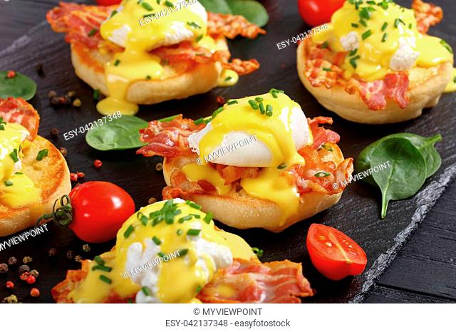 Eggs Benedict - toasted English muffins, fried crispy bacon, poached eggs and classic buttery hollandaise sauce topping sprinkled with finely chopped chives...