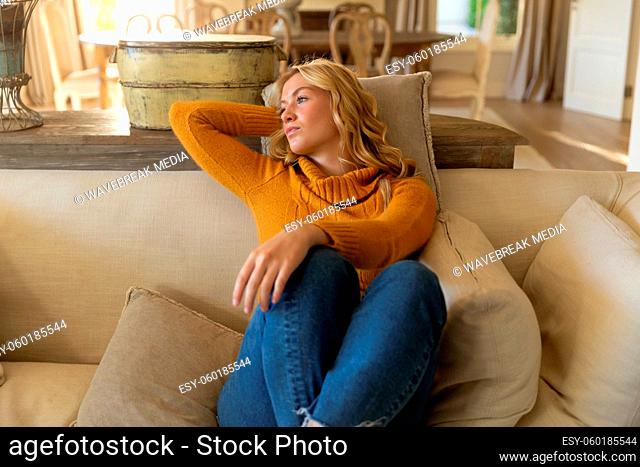 Thoughtful caucasian woman sitting on couch relaxing in luxury living room, looking away