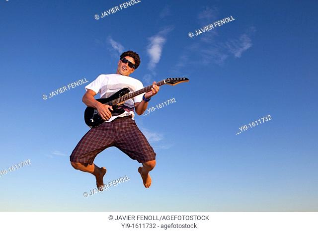 Young man jumping with electric guitar