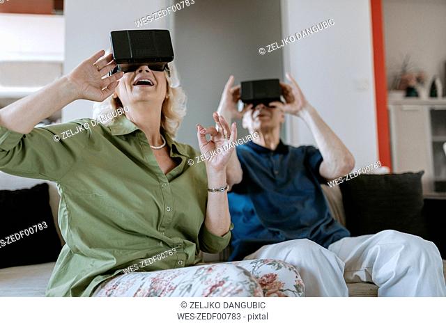 Happy senior couple at home sitting on couch wearing VR glasses