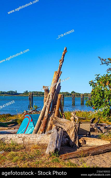 Small tent and chair with driftwood on the banks of the Fraser River estuary in Richmond British Columbia Canada