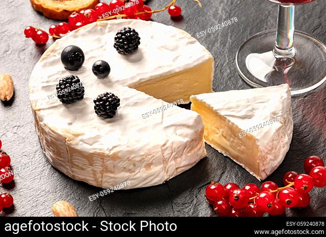 A photo of Camembert cheese with a glass of wine and fruits, on a black background