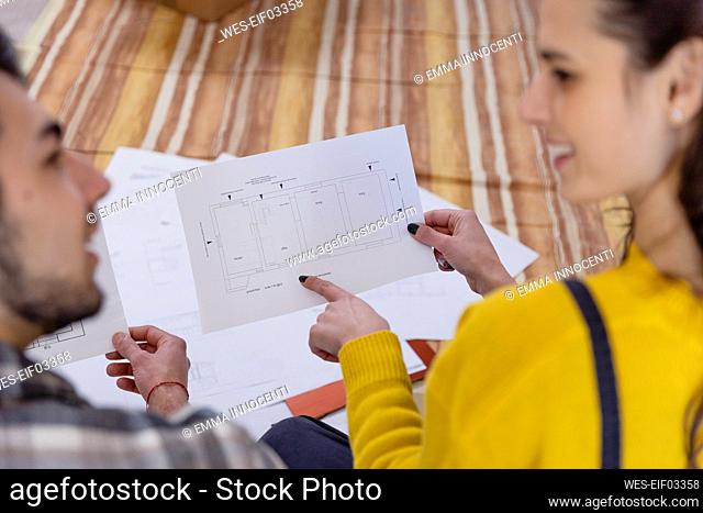 Young woman pointing at floor plans by boyfriend at new home