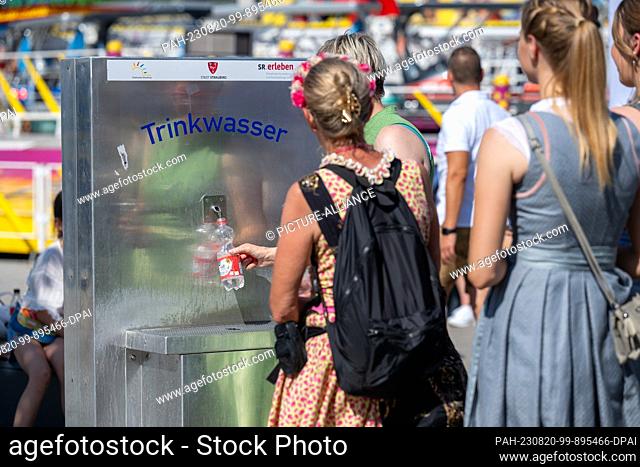 PRODUCTION - 14 August 2023, Bavaria, Straubing: A woman fills free drinking water into a bottle on the grounds of the Gäubodenvolksfest
