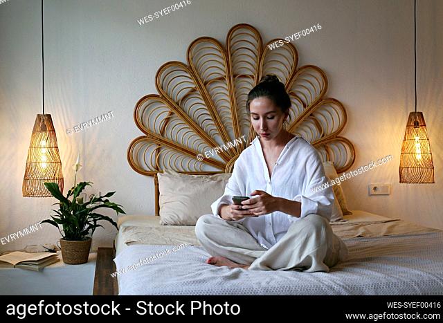 Young woman using smart phone sitting on bed at home