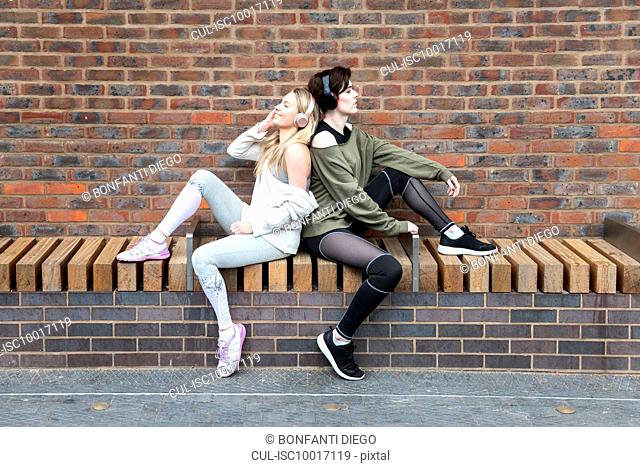 Friends relaxing, two girls listening to music on headphones on a street
