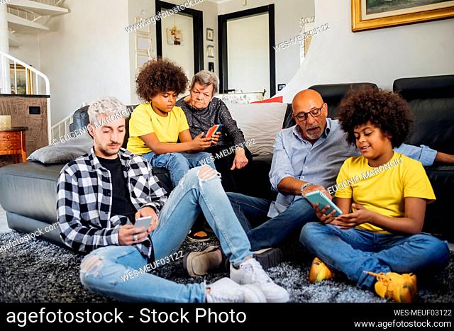 Multiethnic family using smart phones while sitting together in living room at home