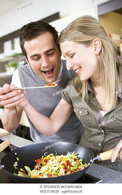 Young couple tasting vegetables from wok