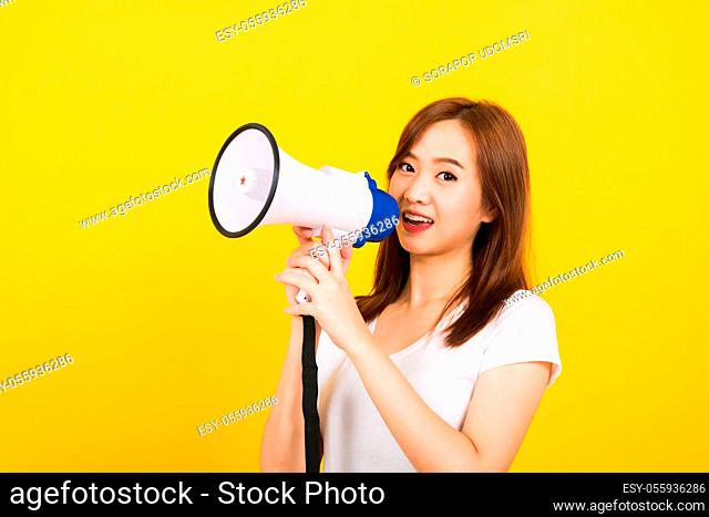 Asian happy portrait beautiful cute young woman teen standing making announcement message shouting screaming in megaphone looking to camera isolated
