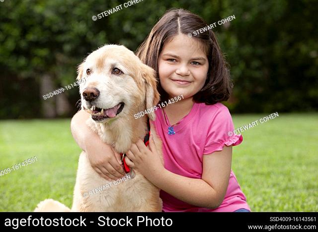 Portrait of young girl and her young golden retriever in backyard