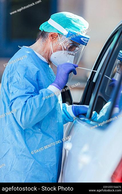 Medical personnel wearing a PPE, performing PCR with a swab in their hand, on a patient inside his car to detect if he is infected with COVID-19