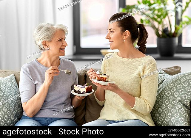 old mother and adult daughter eating cake at home