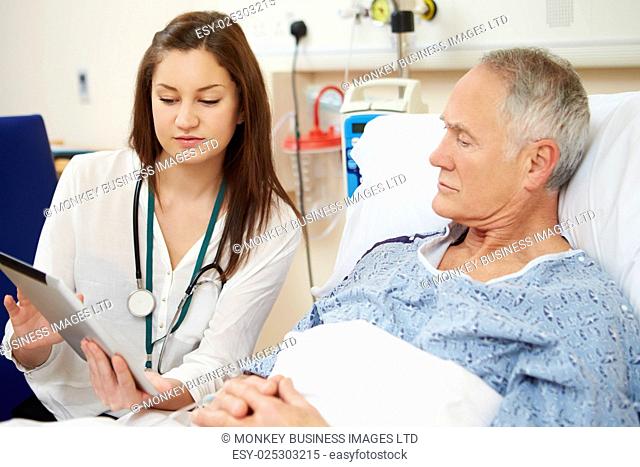 Doctor Sitting By Male Patient's Bed Using Digital Tablet