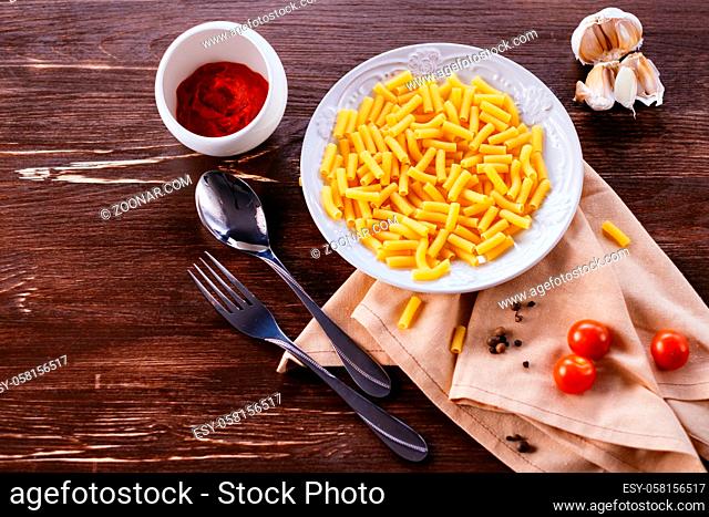 Ingredients for pasta on a wooden table. Plate, cutlery, pasta and fresh vegetables top view