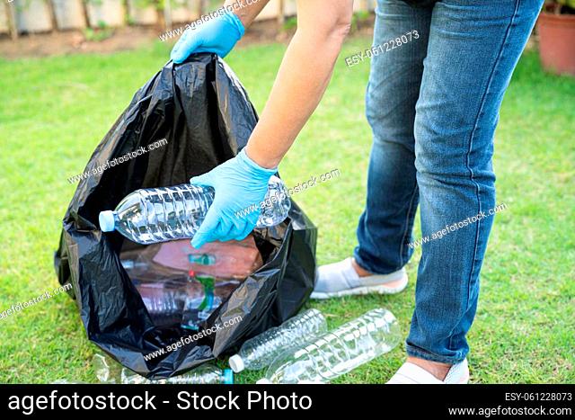 Asian woman volunteer carry water plastic bottles into garbage bag trash in park, recycle waste environment ecology concept
