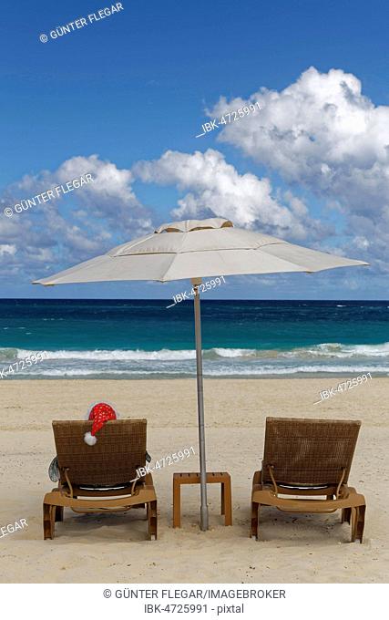 Woman with Santa hat in deck chair with parasol on the beach, Playa Bavaro, Punta Cana, Dominican Republic