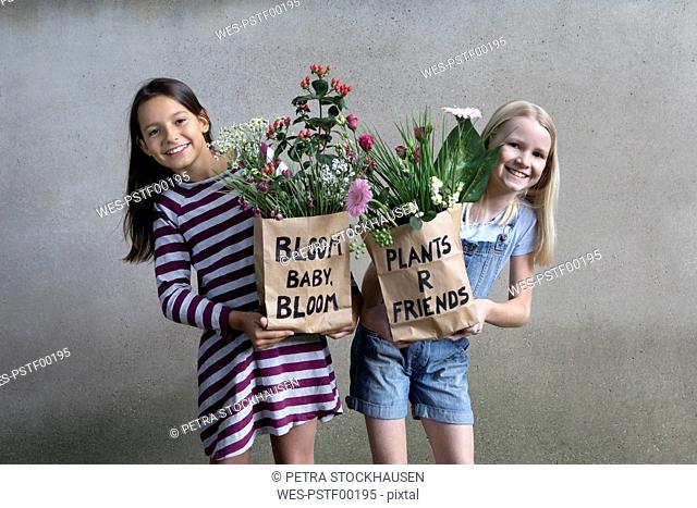 Portrait of two smiling girls holding paper bags with flowers