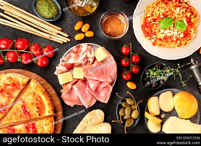 Italian food. Pizza, pasta, cheese, ham, wine, olives, pesto, olive oil, capers, shot from above with a place for text, a flat lay on a dark background