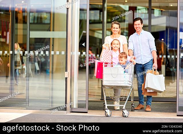 Glückliche Familie und zwei Kinder im Einkaufswagen mit vielen Einkaufstüten
