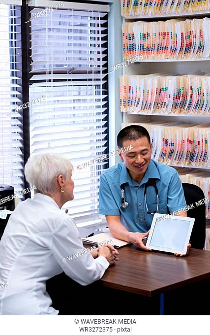 Young Asian male doctor and senior patient discussing over digital tablet in the clinic