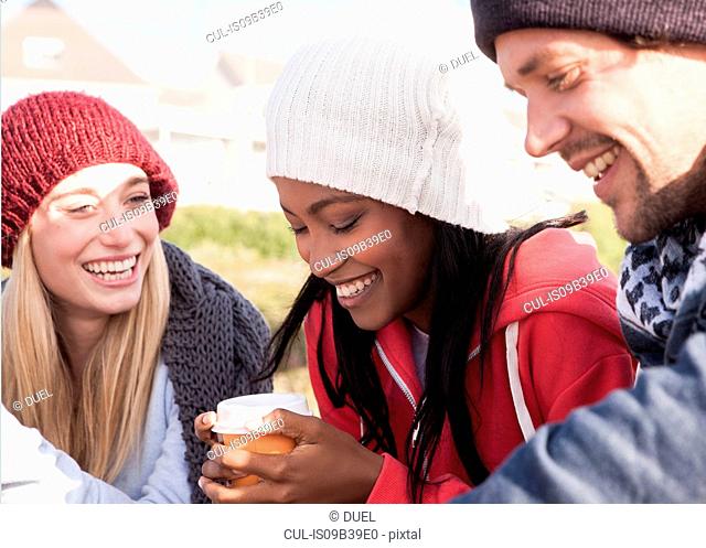 Young adult friends crouching on beach with coffee takeaway, Western Cape, South Africa