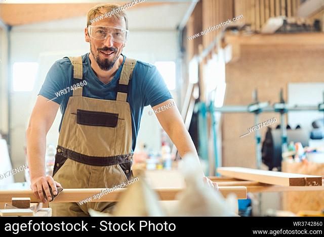 Happy carpenter in his wood workshop looking into the camera