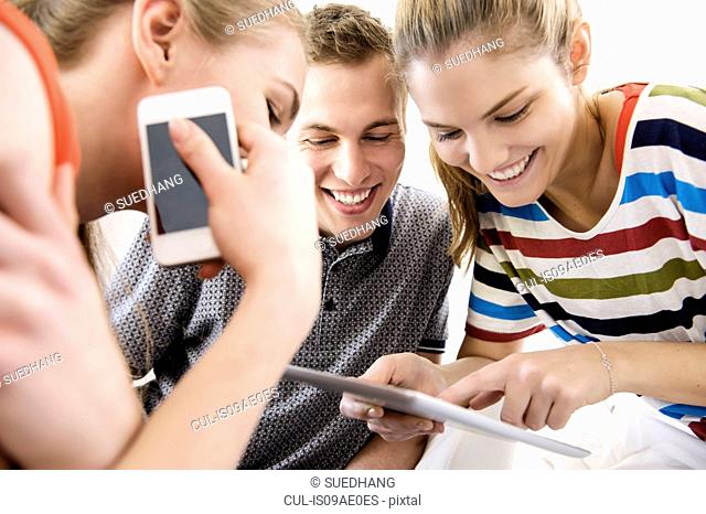 Three young adult friends looking at digital tablet