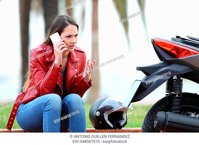 Portrait of an angry biker calling insurance beside a motorbike outdoors in the street