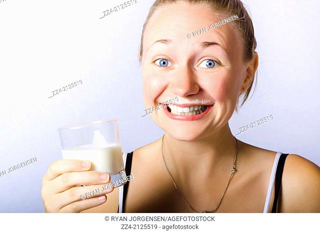Humorous studio image of a happy woman holding glass of milk with creamy top lip smile