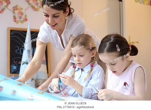 Woman helping her two daughters to decorate cardboard cone