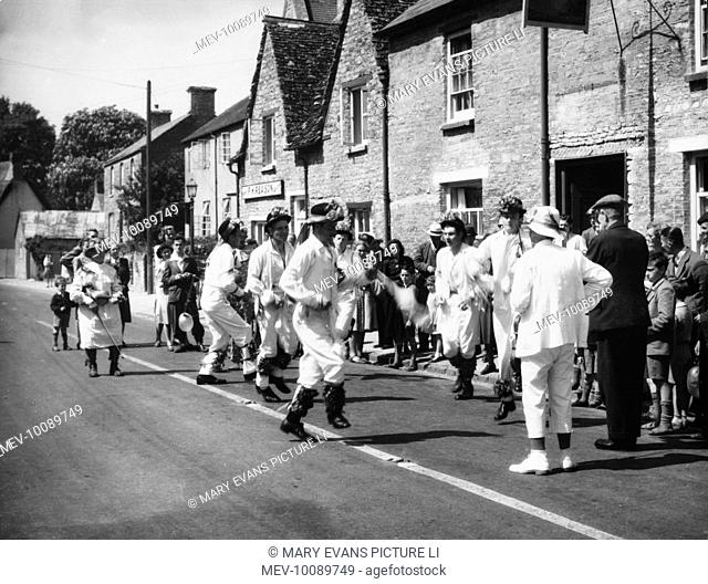 MORRIS DANCING: Bampton, Oxfordshire. Villagers watch a morris dancing team perform in the middle of a road outside a pub on a sunny Whit Monday