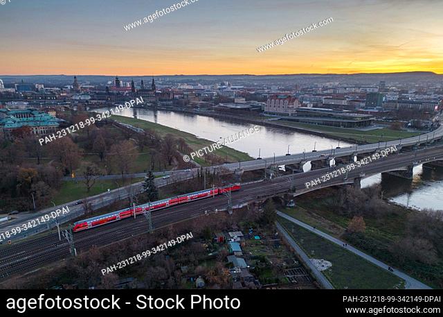 17 December 2023, Saxony, Dresden: An S-Bahn train crosses the Elbe on the Marienbrücke bridge in the evening against the backdrop of the old town