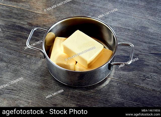 ayurvedic diet, steps to prepare homemade ghee from butter - three pieces of organic sour cream butter in a stainless steel cooking pot on a dark wooden...