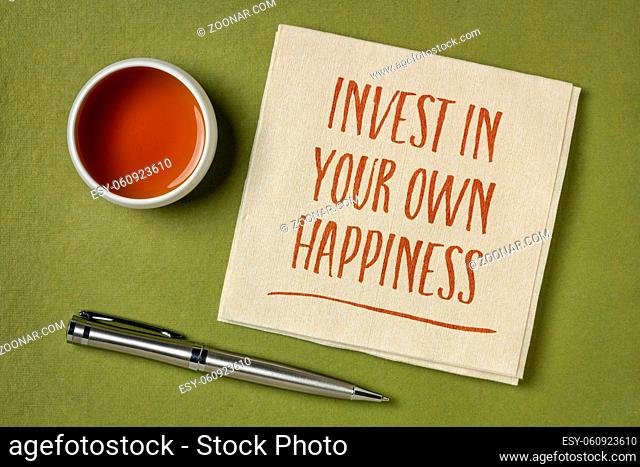 invest in your own happiness - handwriting on a napkin with a cup of tea, lifestyle and personal development concept