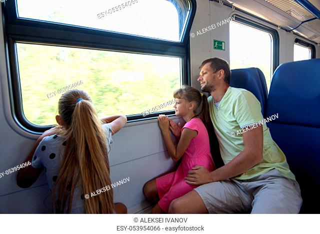 Dad and two daughters in an electric train car, look out the window with enthusiasm