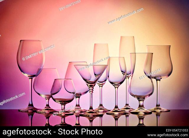 Set of glasses for different alcoholic drinks and cocktails on light pink-yellow background. Empty clear glassware