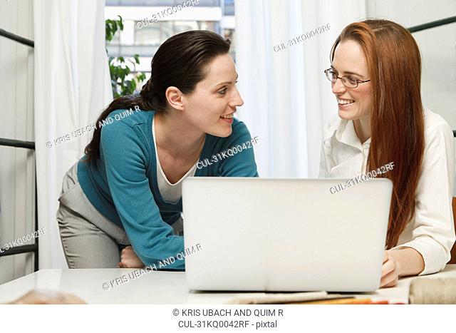 2 women smiling at each other, behind a laptop