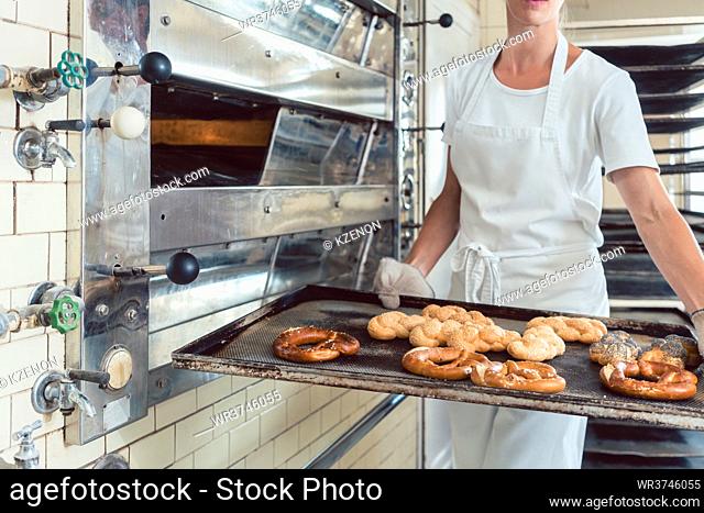Baker is presenting freshly baked bread on tray in her bakery shop