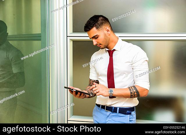 Handsome young businessman in his office working and using tablet PC, looking down, serious
