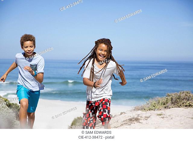 Playful brother and sister running on sunny summer ocean beach