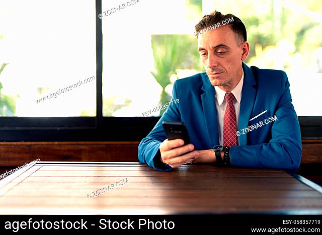 Portrait of mature handsome Italian businessman relaxing at the coffee shop